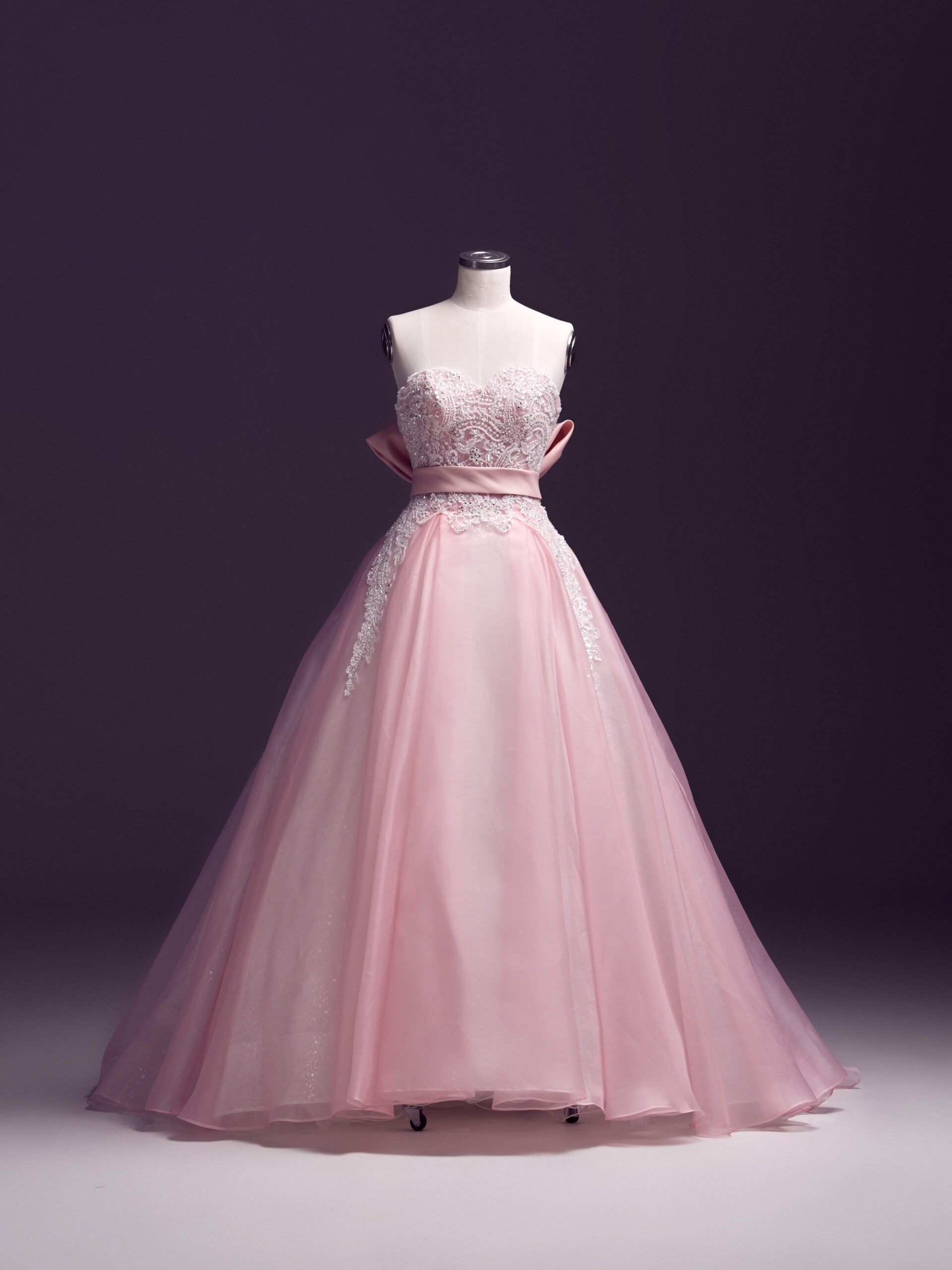 A strapless, floor-length pink ball gown with a fitted bodice, lace detailing, and a full tulle skirt displayed on a headless mannequin against a dark background.